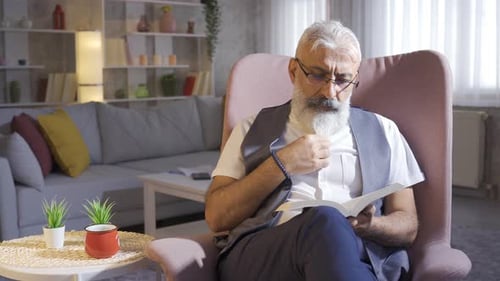 Silver Haired Man Reads Book in Comfortable Armchair