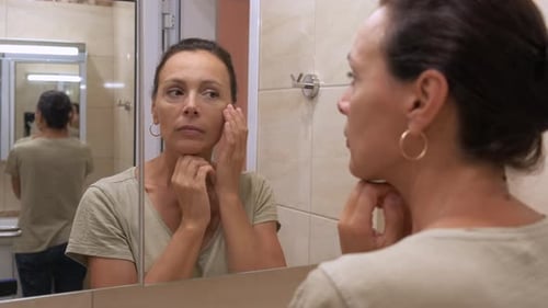 Woman Looks in Mirror and Examines Her Face