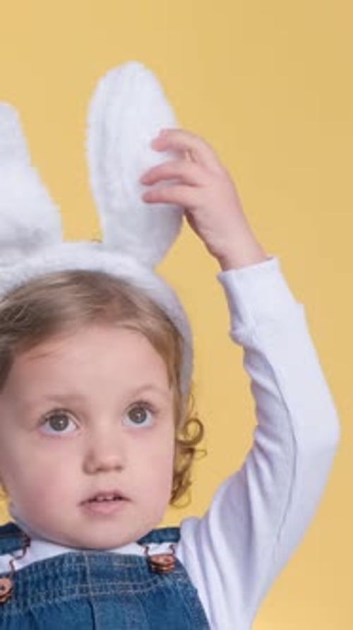 A Cute Little Girl with Easter Bunny Ears on a Yellow Background Shows Different Emotions