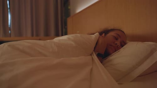 Hotel Bed with Peaceful Guest Cuddling Pillow Warm Bedside Glow Closed Curtains Soft Duvet Pulled