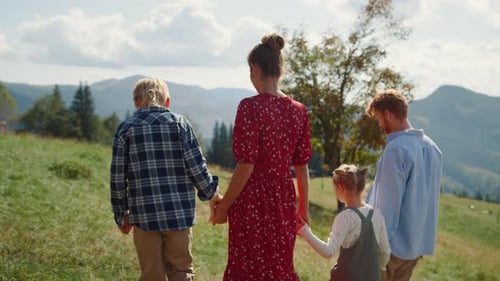 Family Spending Vacation Together On Green Sunny Meadow. Unknown Parents Walking Green Grass With...