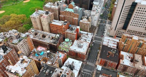 Flying over the residential area and avenue in New York. Green park near the buildings at backdrop.