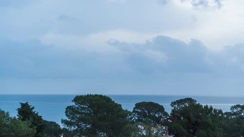 Zeitraffer eines Sonnenaufgangs über dem Meer durch Regenwolken, der sie teilweise in warmen Farben färbt.