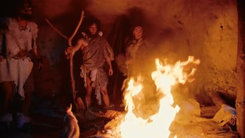 Tribe of Prehistoric Hunter-Gatherers Wearing Animal Skins Stand Around Bonfire Outside of Cave at