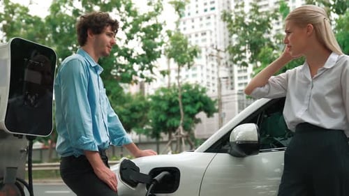 Progressive businessman and businesswoman use charging station for EV car.
