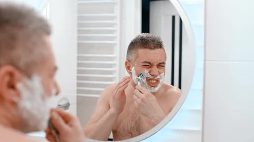 Adult Man Shaving in Bright Bathroom Mirror