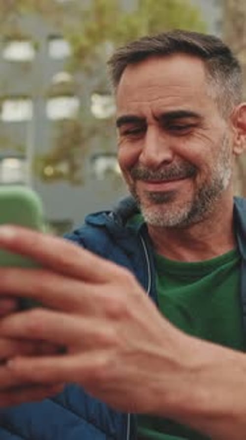 Close up, middle-aged man sits on bench in the park uses mobile phone