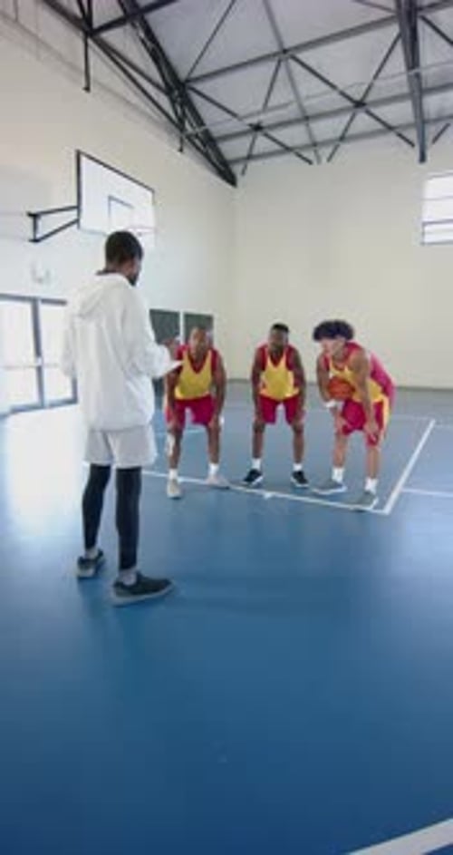 Vertical video: Basketball coach instructing male players on court during practice session