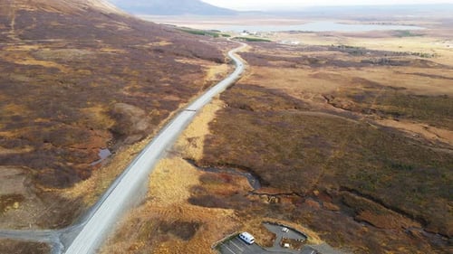 Stunning aerial of car driving over a long road through a gorgeous Icelandic landscape.