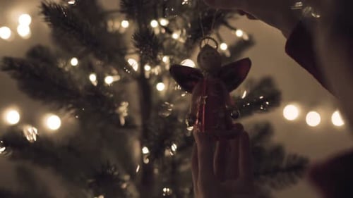 Hands Decorating Christmas Tree With Angel Ornament