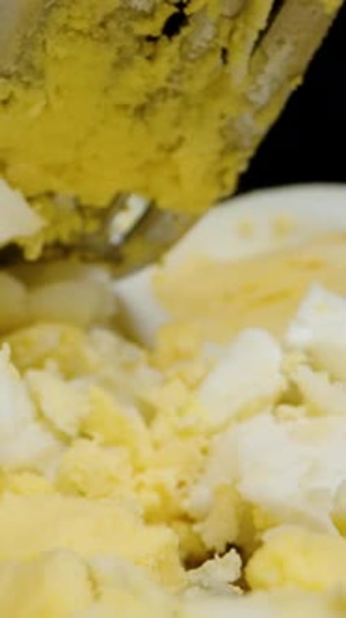 Vertical video. Crushed boiled chicken eggs with a fork on a wooden table. Dolly slider, close-up.
