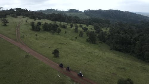 4k panning Aerial shot over a group of motorcycle rider crossing a dirt road on a hill top country s