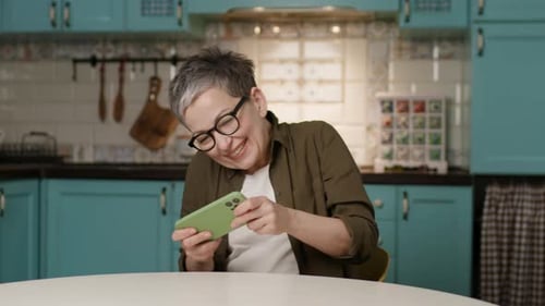 Enthusiastic Woman Gaming on Smartphone at Kitchen Table