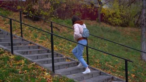 Young woman climbs stairs in park in autumn. Stock footage. Beautiful young woman walks in park