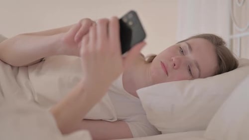 Side View of Young Woman using Smartphone in Bed
