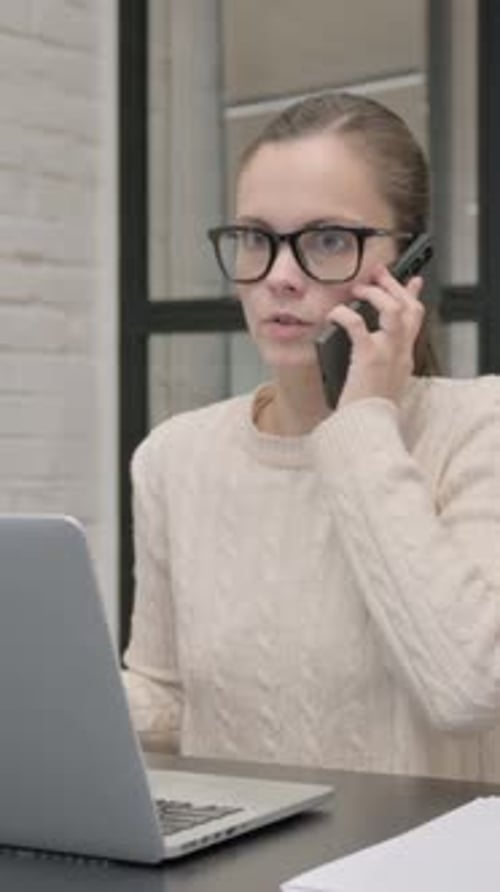 Woman talking on phone while working at laptop
