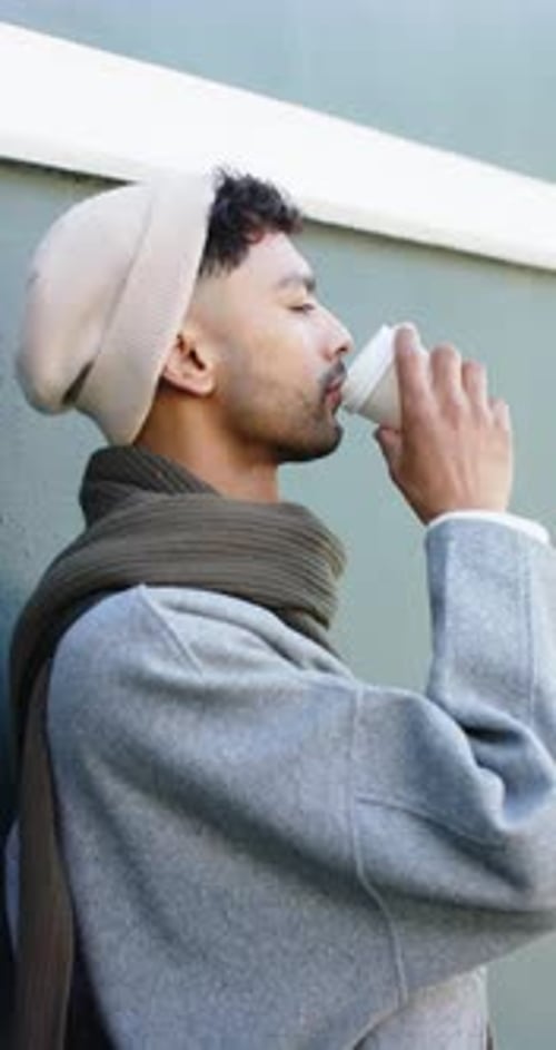Vertical video: Adult male raising coffee cup to lips smiling while sipping for warmth on street