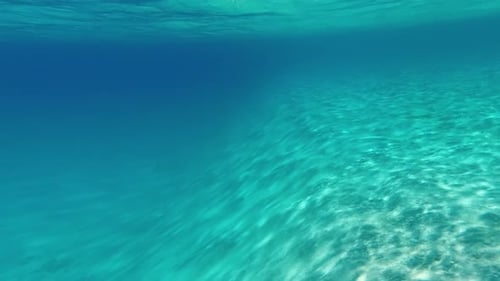 Underwater view: Steep sandy slope, sun reflects off turquoise bottom