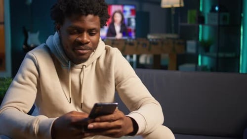 African American Man on a Sofa Texting Mates in His Living Room