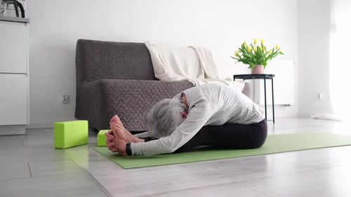 Senior Woman Stretching and Touching Toes on Yoga Mat
