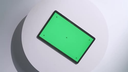 Top down view of a mock up green screen tablet rotates on a white desk