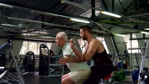 Trainer Helping Senior Man with Squats at Gym