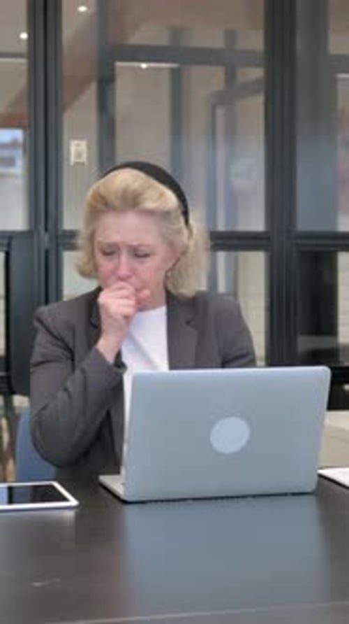 Woman Coughing in Front of Laptop at Desk