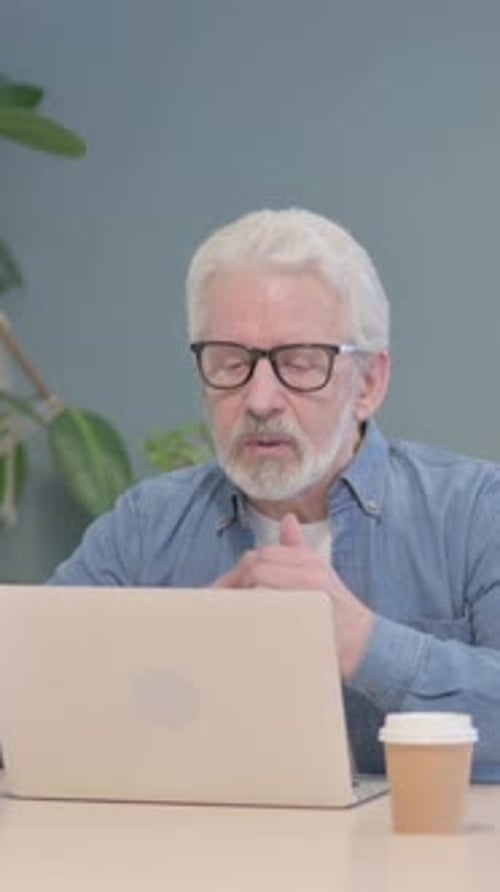 Senior Man Video Conferencing on Laptop at Desk
