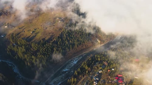 Vista aérea del vibrante paisaje de nubes brumosas que cubren las colinas de las montañas y un pequeño pueblo disperso