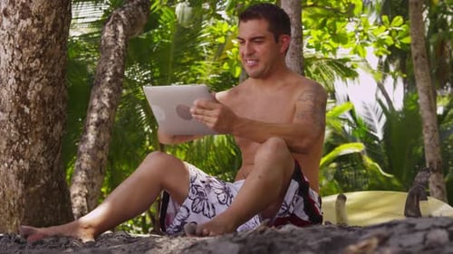 Surfer relaxes on costa rica beach with tablet enjoying tropical vacation