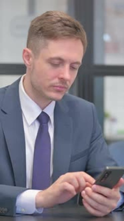 Vertical video, Mature Adult Businessman Browsing Internet on Phone in Office