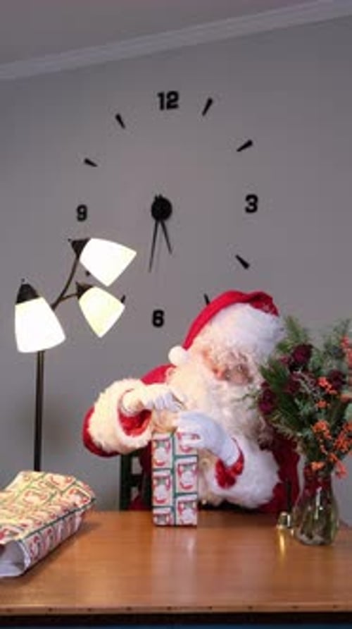 Santa Claus Wrapping Christmas Gifts Indoors at Table