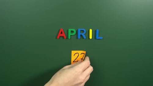Hand sticking a sticker 27 April calendar day on school board. 27 date of April. Twenty seventh day