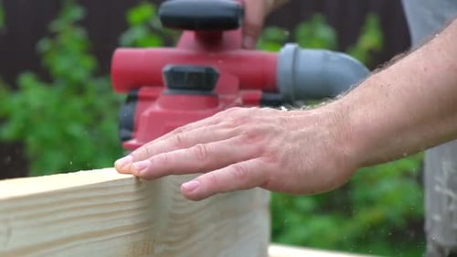 Male Carpenter Using Electric Circular Saw in Backyard Workshop with Wood Chips Flying Building
