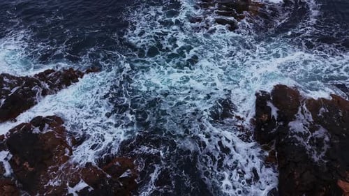 Waves crash against rocks during the day by the ocean shore