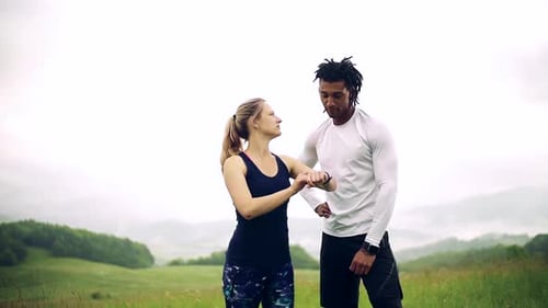 Young couple checks smartwatch fitness progress on foggy meadow after exercise