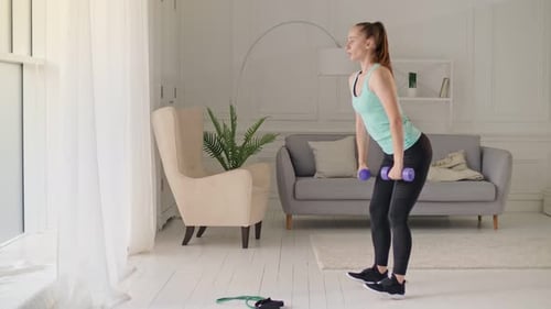 Une fille joyeuse et animée tenant un petit haltère rose et faisant des exercices pour maintenir une activité sportive saine