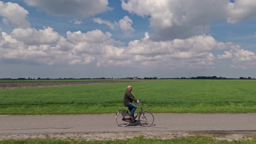 Mann radelt an einem sonnigen Tag mit schönen Wolken durch Frieslands Wiesen