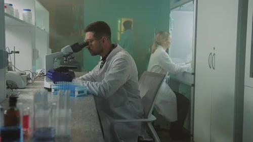 Close Up Scientist with Glasses and Protective Gloves Looking in the Microscope in the Laboratory