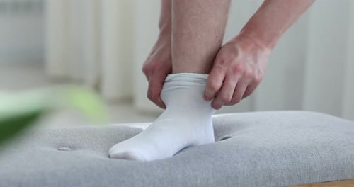 Man Pulling on a White Sock on Ottoman