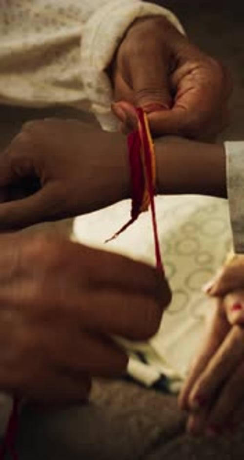 Écran vertical : Gros plan authentique d'un prêtre hindou attachant un fil mauli autour du poignet d'un enfant de sexe masculin