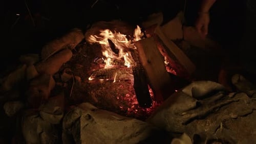 Slow motion crackling campfire being tended to with firewood and embers flying off