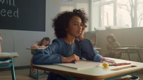 Pensive african american schoolgirl sits at desk thinking at elementary school