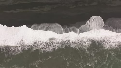 Aerial shot of waves crashing against the black sand beach of Reynisfjara, Iceland, highlighting the