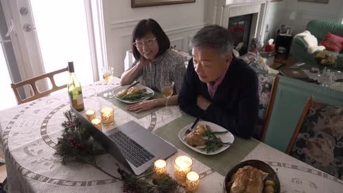 Cheerful senior couple connects with family on laptop video call at lunchtime in Canada