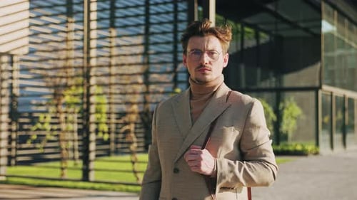 Serious Man with Glasses in Coat Stand Look at Camera Near Modern Architecture at Sunlight Portrait