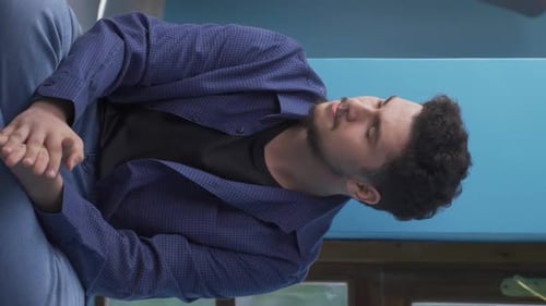 Vertical video of The man sitting on the ground is crying. Downhearted.