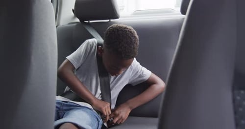 African American boy buckles up in the backseat of a car
