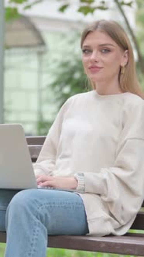 Woman Sitting on Bench Working on Laptop Smiling