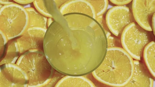 Pouring Orange Juice into Glass Surrounded by Slices